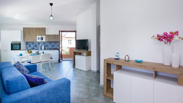 A modern living room with a blue sofa, a wooden coffee table, and a TV in the background. - Holiday Home "Casa Michela" with 2 Balconies and Wi-Fi (Orosei)
