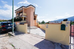 Un immeuble résidentiel doté d’une entrée sécurisée par un portail, d’un escalier menant à l’entrée et d’une boîte aux lettres fixée au mur.