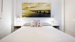 A hotel room with a bed, a nightstand, a wall-mounted lamp, and a painting of a pier.