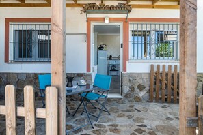 A stone patio with a table and chairs, a wooden gate, and a view into a kitchen area.