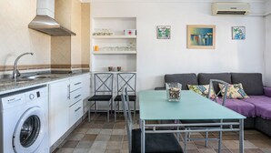 A compact living space with a washing machine, a dining table, a sofa, and a small kitchen area with a sink and cabinets.