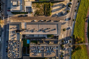 An aerial view of a parking lot with multiple rows of parked cars, a pedestrian crossing, and a building with a flat roof.