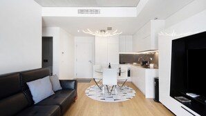 Un salón moderno con un sofá de cuero negro, una mesa de comedor blanca y una cocina al fondo.
