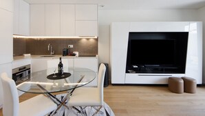 Una cocina moderna con una mesa de comedor de vidrio, armarios blancos y un televisor de pantalla plana grande.