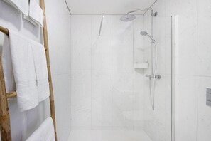 Un espace douche doté d’une porte en verre, d’un porte-serviettes en bois et d’un pommeau de douche à main.