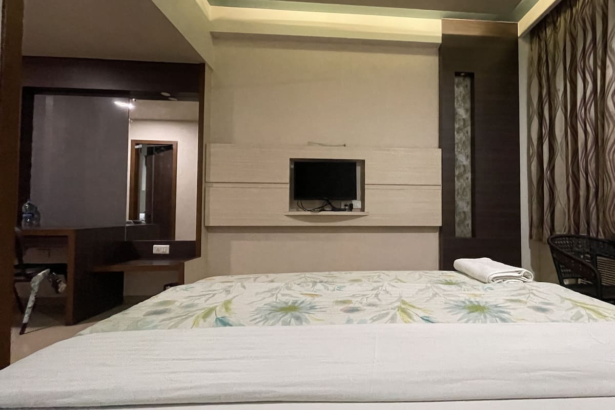 A hotel room with a bed, a television mounted on the wall, a chair, and a small table.