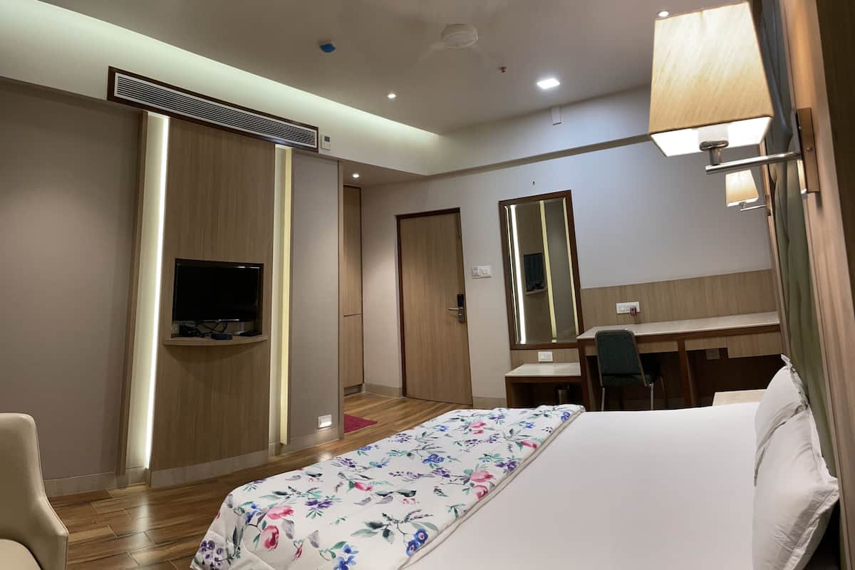A hotel room with a bed, a desk, a chair, a television, a mirror, and a lamp.