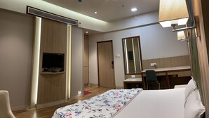 Una habitación de hotel con cama, escritorio, silla, televisión, espejo y lámpara.