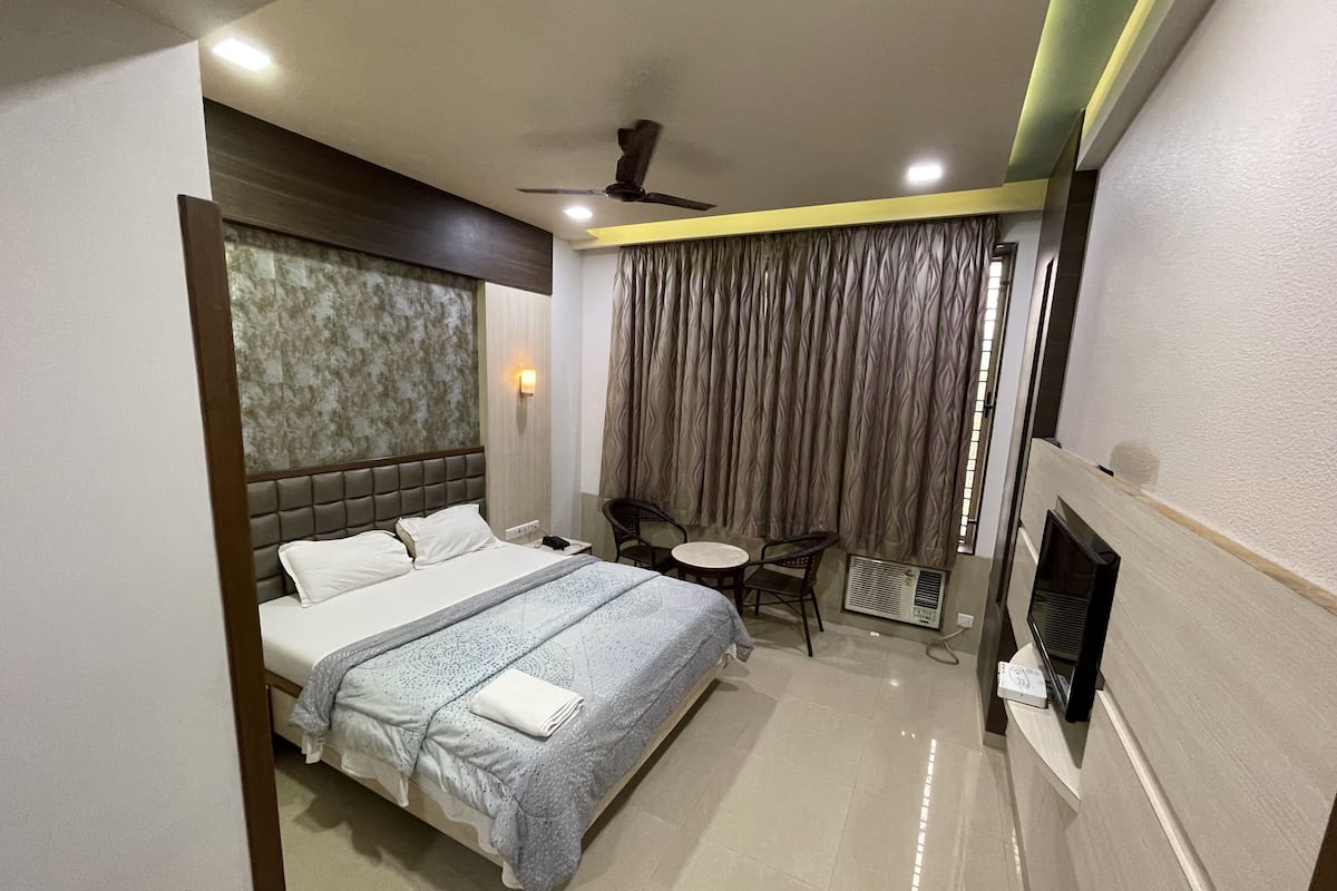 A hotel room with a bed, a small table, two chairs, a ceiling fan, and a wall-mounted TV.