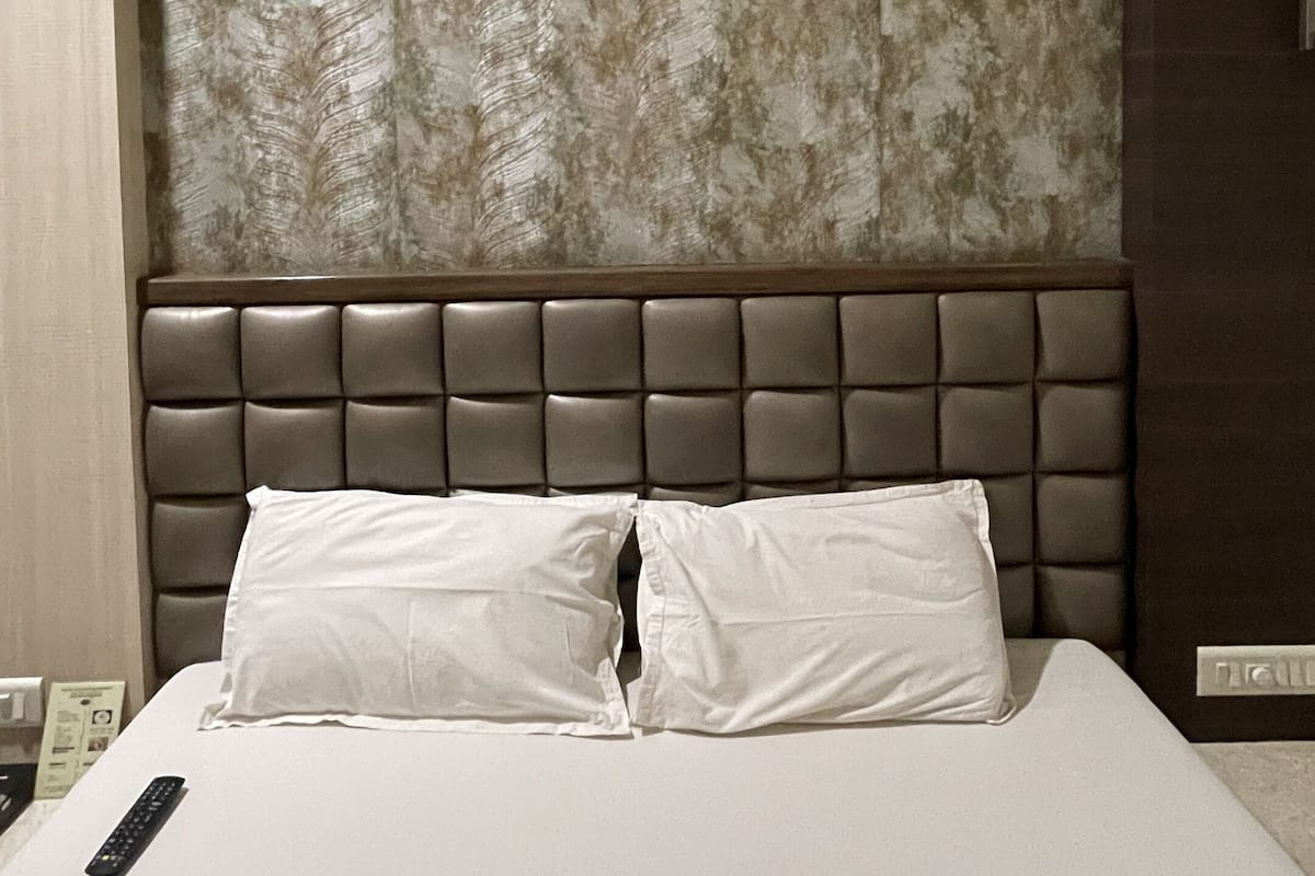 A hotel room with a large bed, a headboard with a textured panel, and a wooden door.
