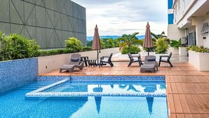 A rooftop pool area with lounge chairs and umbrellas, surrounded by greenery and a modern building facade. - Inspiria Fully-Furnished Studio Unit with Balcony (Davao City)