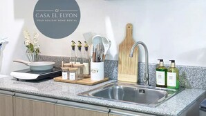 A modern kitchen with a granite countertop, stainless steel sink, and wooden cutting board. There are jars of spices, a pot, and a vase with flowers. - Inspiria Fully-Furnished Studio Unit with Balcony (Davao City)