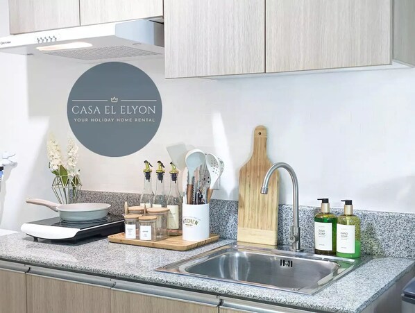 A modern kitchen with a granite countertop, stainless steel sink, and wooden cutting board. There are jars of spices, a pot, and a vase with flowers.
