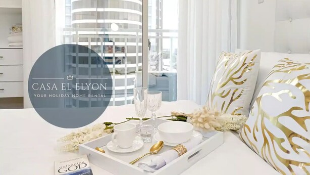 A hotel room with a large window, a bed with white and gold patterned pillows, a tray with a cup, glass, bowl, and flowers. - Inspiria Fully-Furnished Studio Unit with Balcony (Davao City)