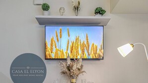 A dining area with a table set for four, a flat-screen TV mounted above it, and a decorative vase with flowers. - Inspiria Fully-Furnished Studio Unit with Balcony (Davao City)