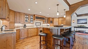 Une cuisine spacieuse avec des meubles en bois, un grand îlot central doté de tabourets et un plan de travail en pierre.