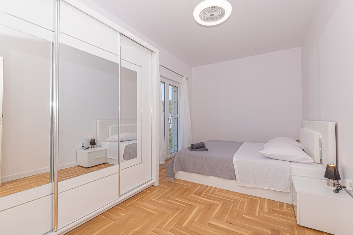 A bedroom with a bed, bedside table, lamp, and a large mirror.