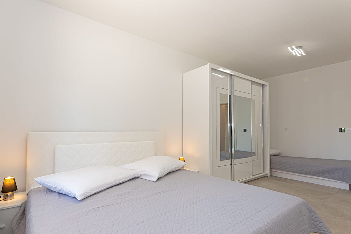 A modern bedroom with a large bed, a wardrobe, and a bedside table with a lamp.