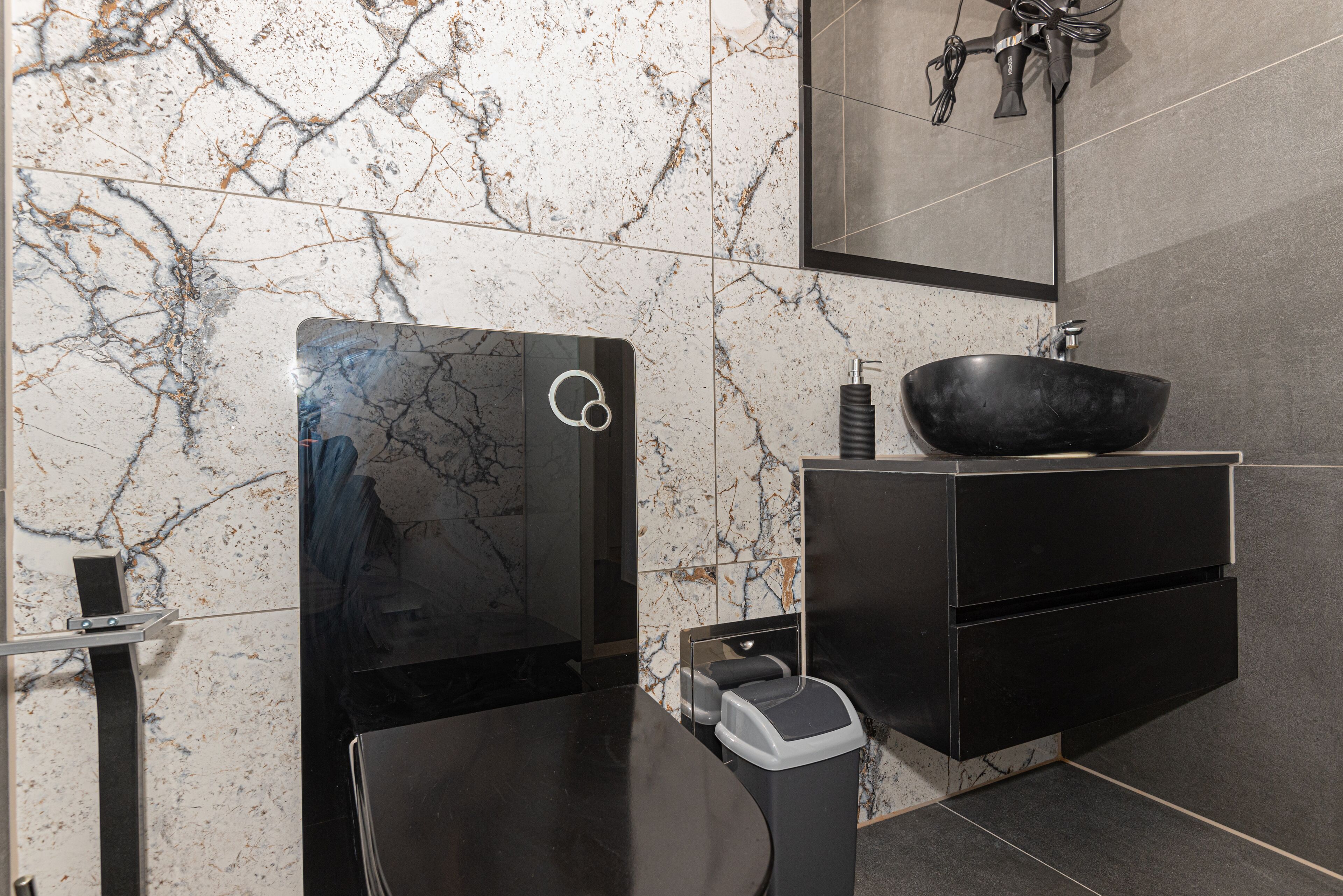 A modern bathroom with a black sink, marble walls, and a mirror above the sink.