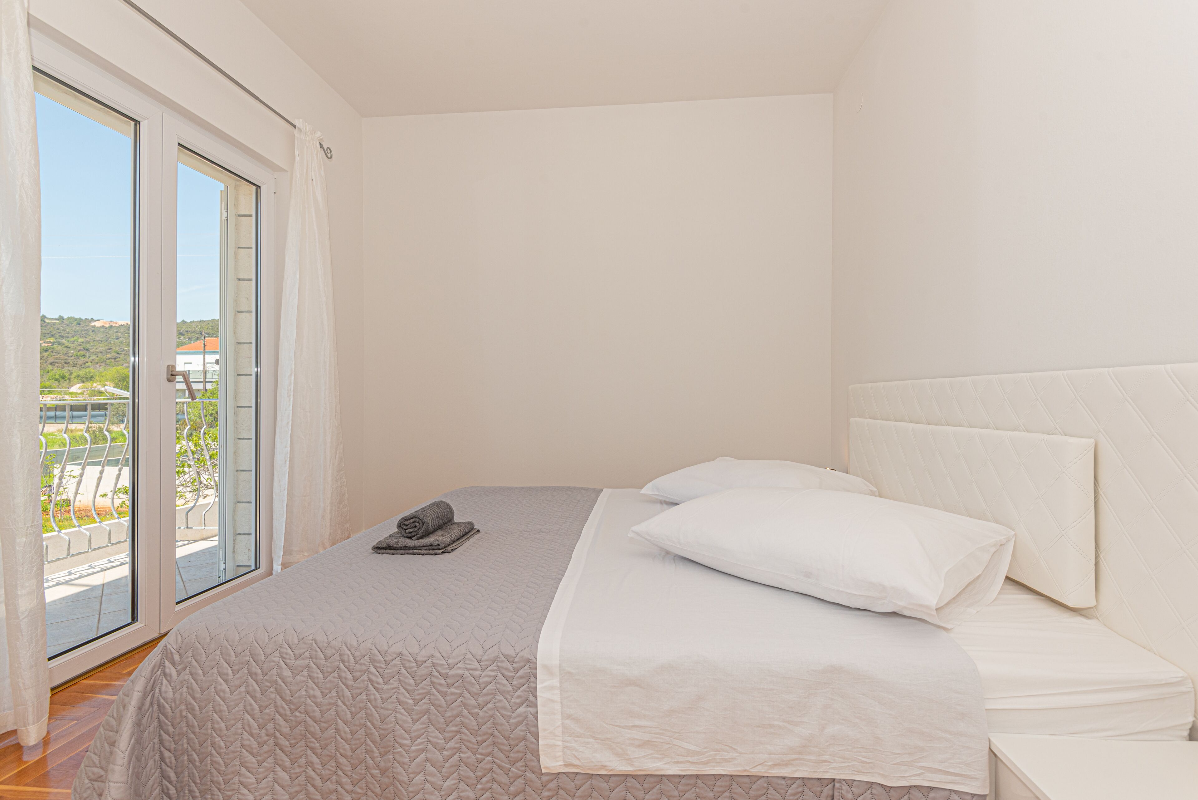 Un dormitorio con cama, vista a través de una puerta corrediza y cabecera blanca.