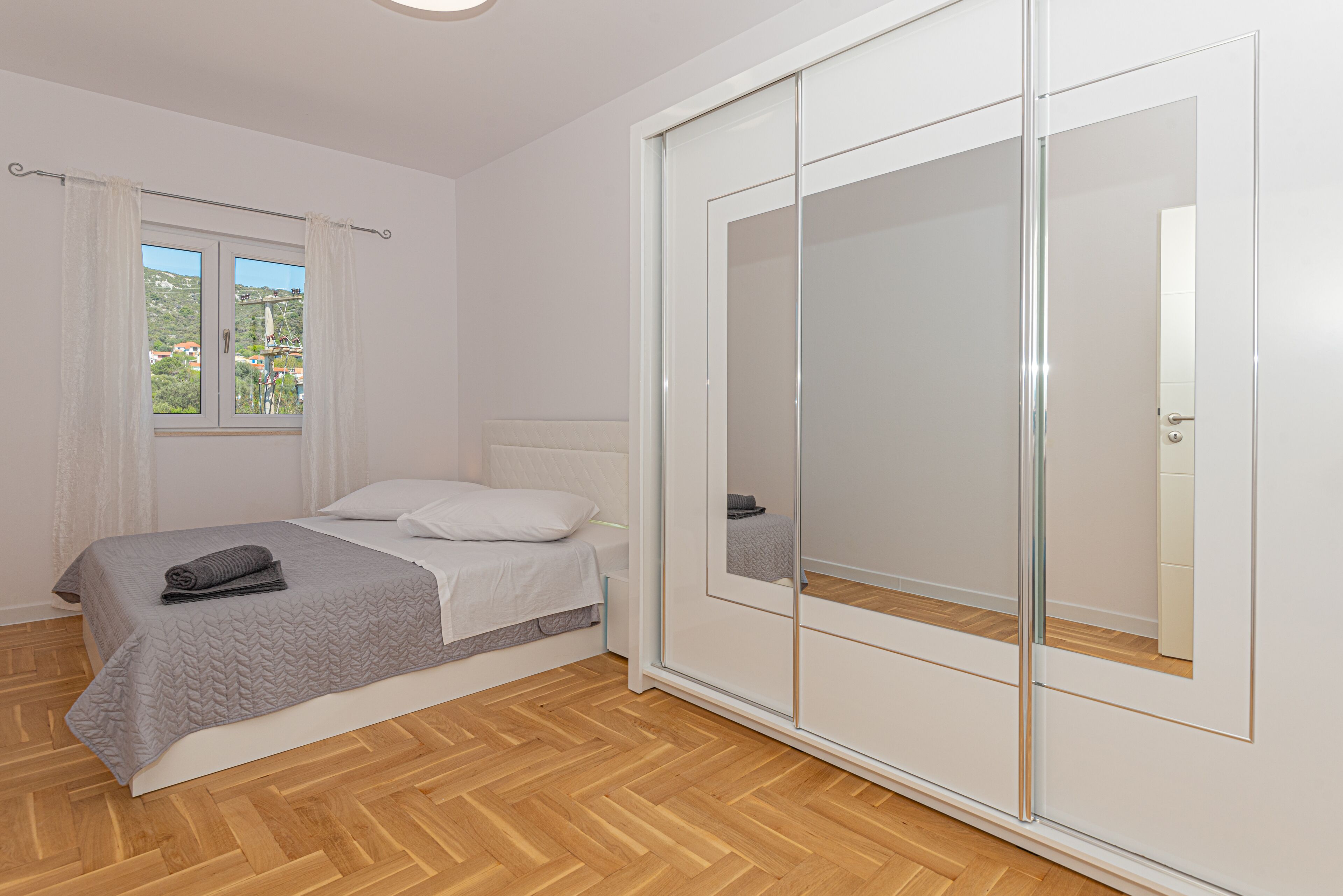A bedroom with a bed, a wardrobe with a mirror, and a window with curtains.