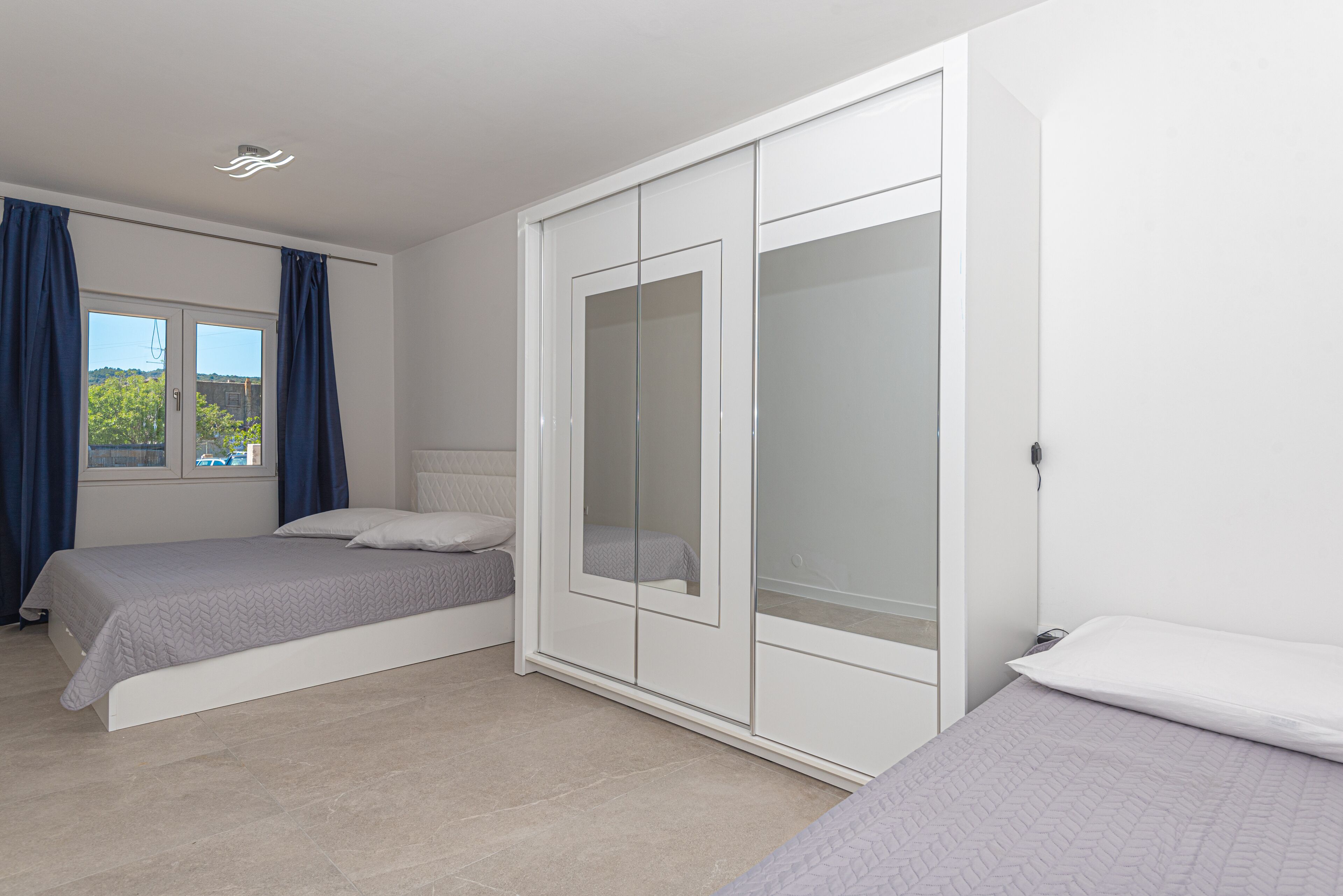 A bedroom with two beds, a wardrobe, and a window with curtains.