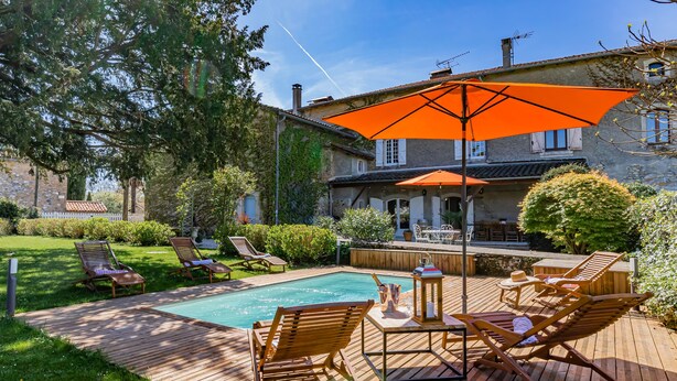 A wooden deck with a pool, lounge chairs, and an orange umbrella.