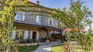 A rustic stone house with a covered patio, potted plants, and a gravel pathway.