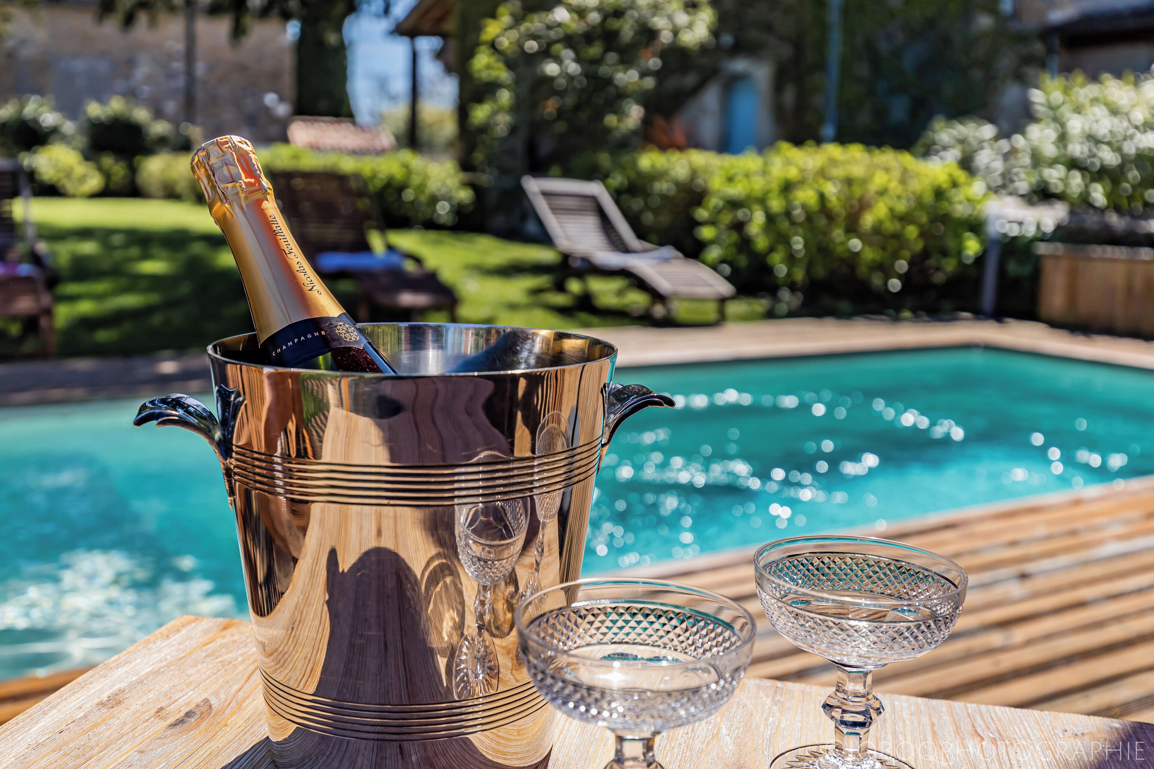 A poolside setting with a champagne bucket, two glasses, and a pool.