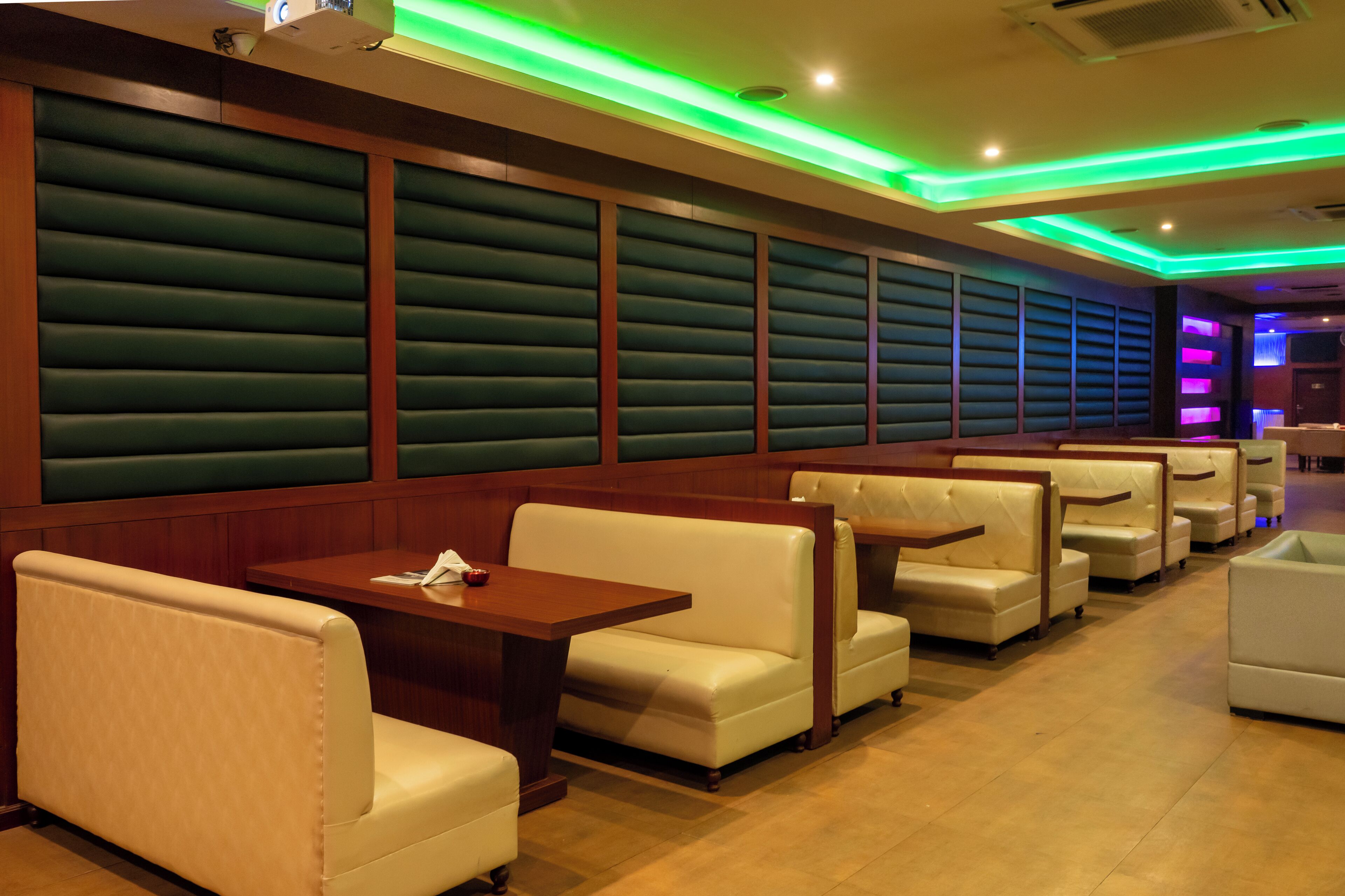 Un ristorante con sedute a cabina e tavoli, pareti imbottite verdi e illuminazione al neon verde e blu.