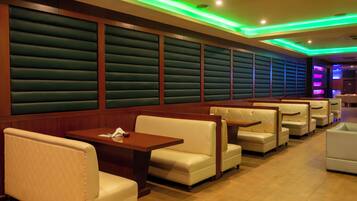 Un ristorante con sedute a cabina e tavoli, pareti imbottite verdi e illuminazione al neon verde e blu.