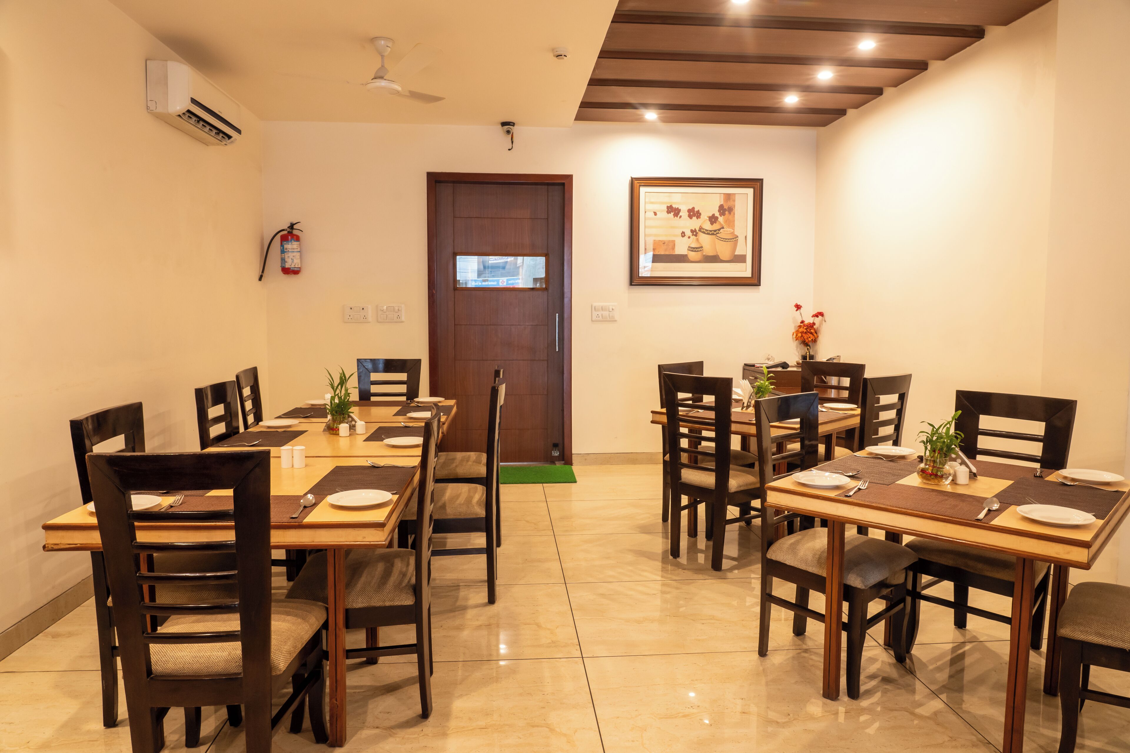A dining area with wooden tables and chairs, a fire extinguisher, and a framed picture on the wall.