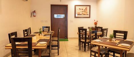 A dining area with wooden tables and chairs, a fire extinguisher, and a framed picture on the wall.