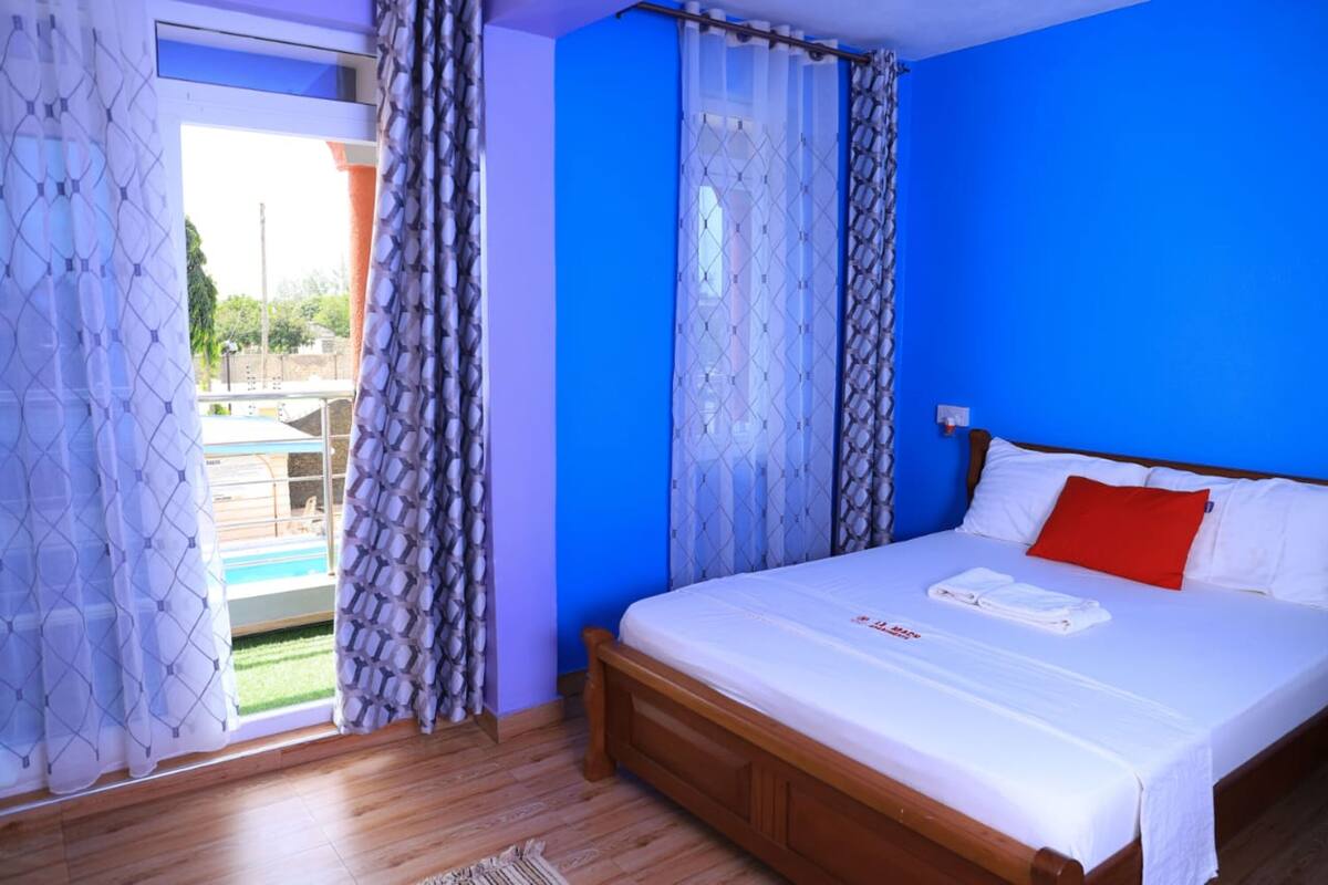 A bedroom with a wooden bed, white bedding, and a red pillow.