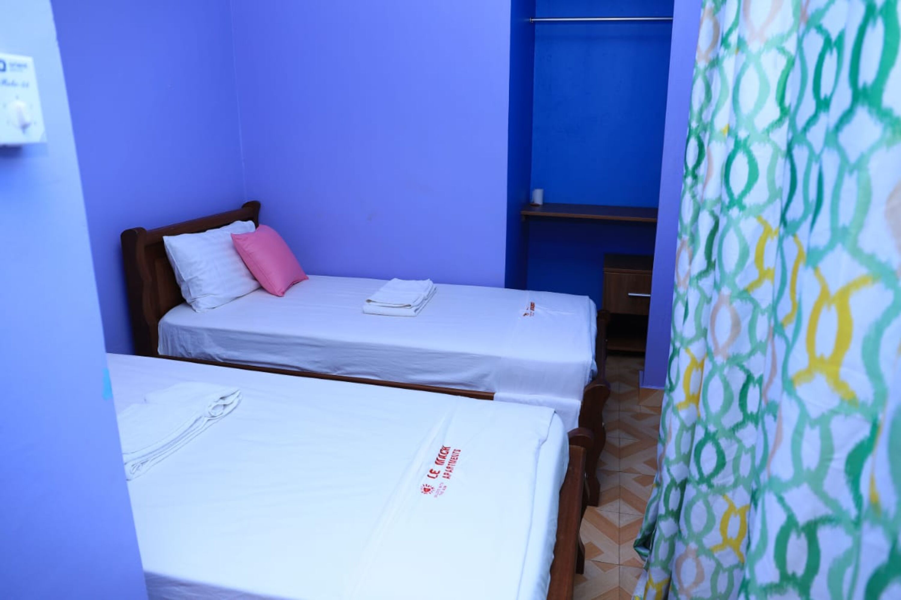 Two single beds with white linens, a wooden headboard, and a pink pillow.