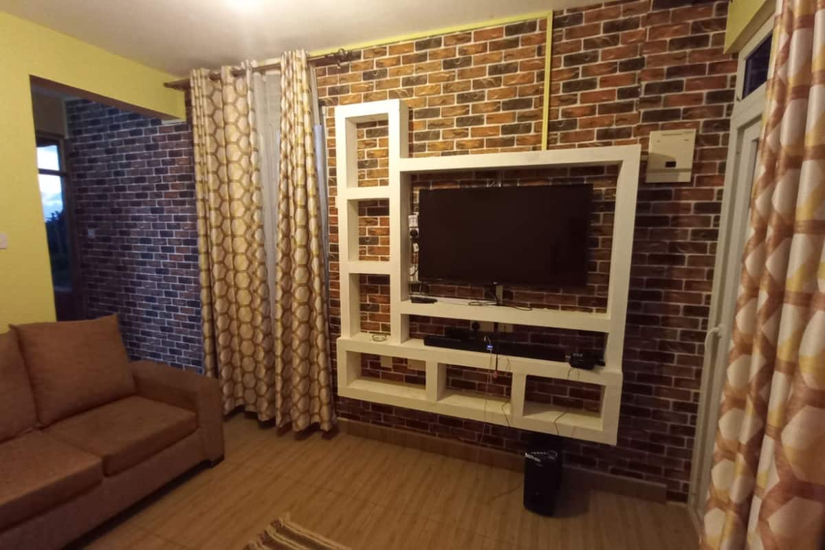 A living room with a brick wall, a mounted TV, a brown sofa, and patterned curtains.