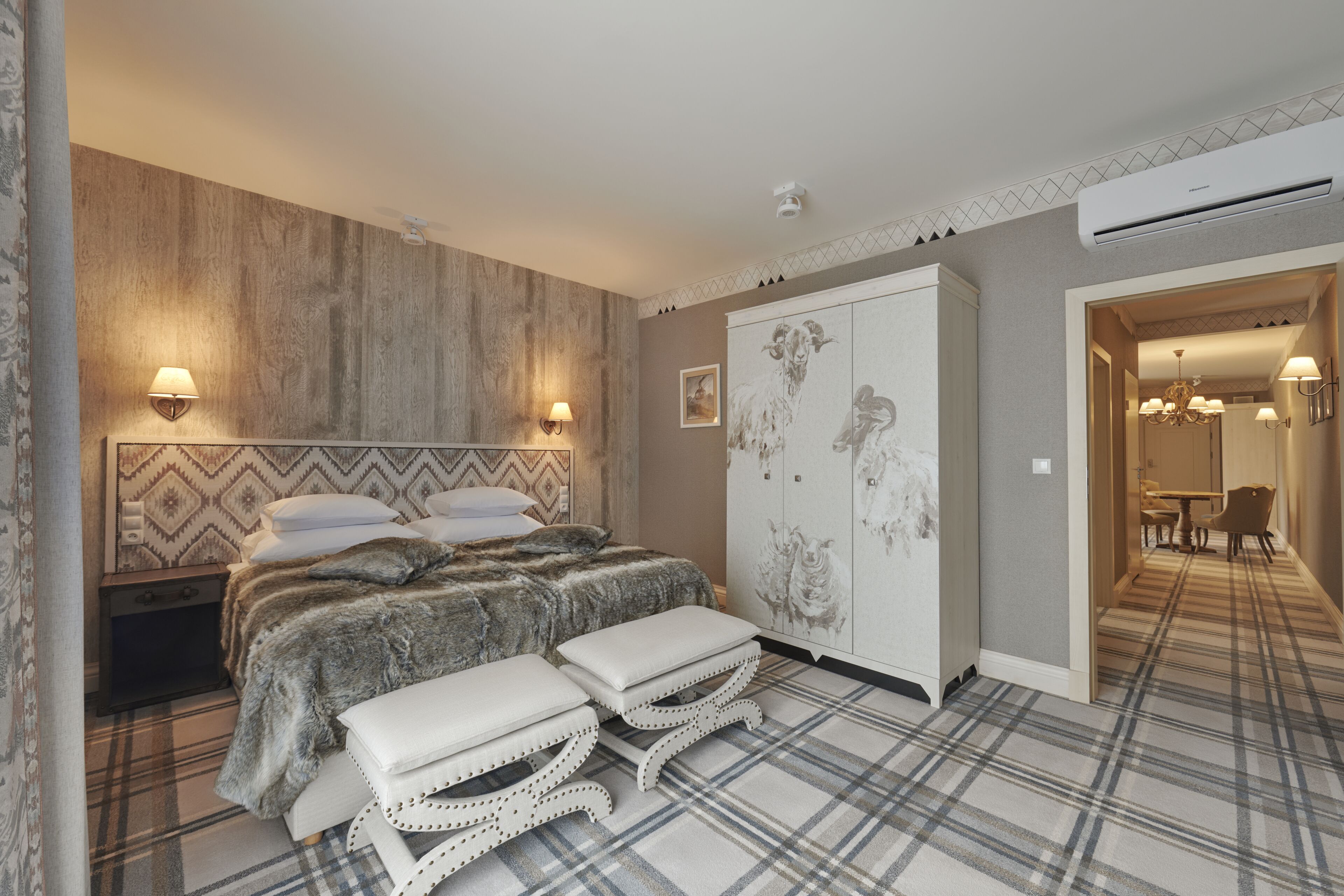 Un dormitorio con una cama grande, dos mesitas de noche, un armario y una zona de comedor con candelabro.