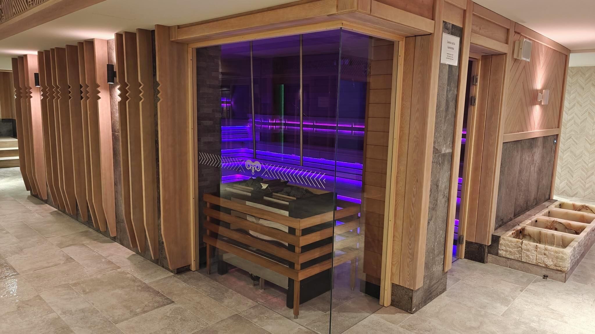Una sauna con cerramiento de vidrio y revestimiento de madera, que incluye un banco y una plataforma de piedra.