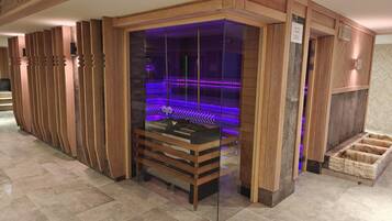 Una sauna con cerramiento de vidrio y revestimiento de madera, que incluye un banco y una plataforma de piedra.