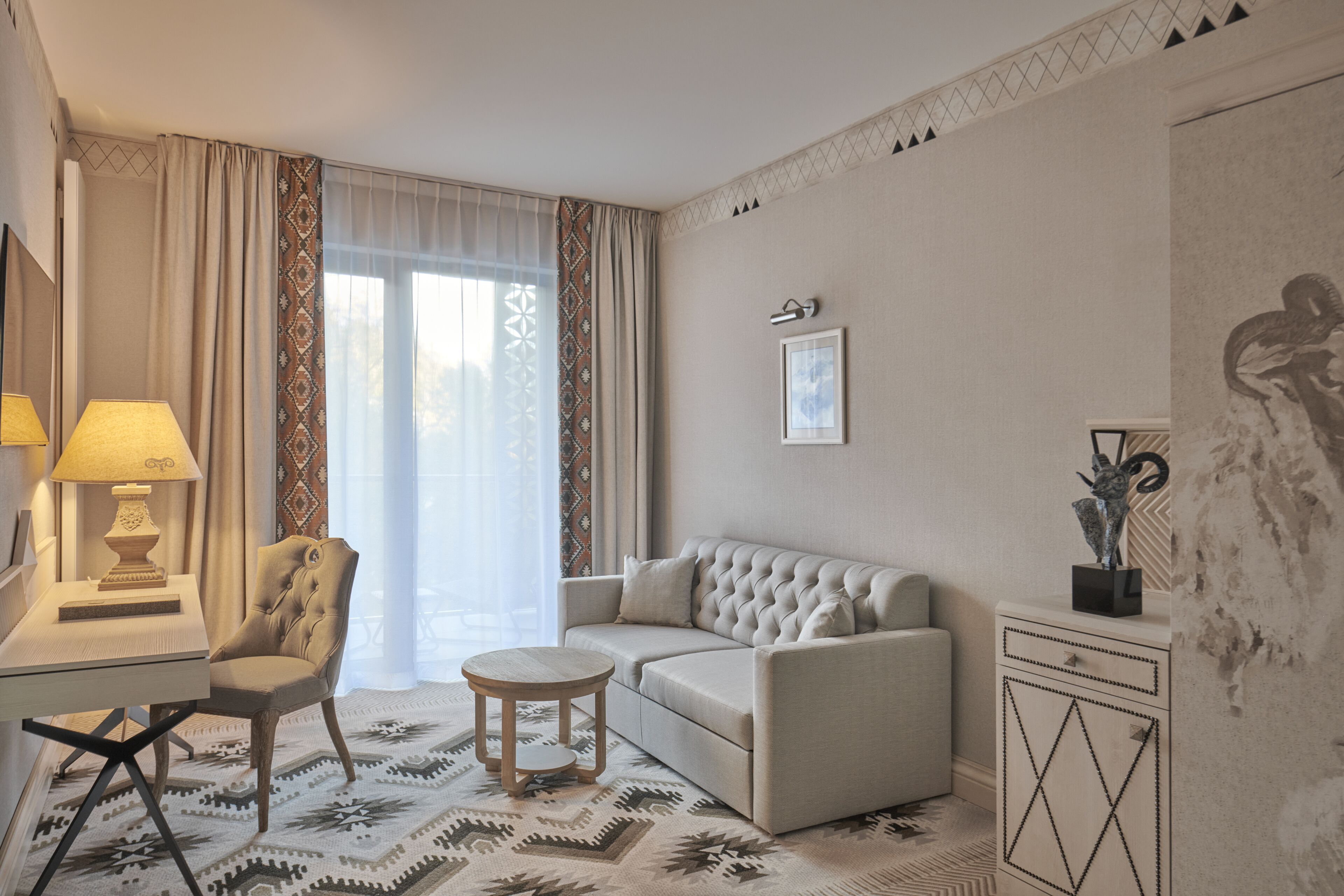 Una habitación de hotel con sofá, sillón, mesa redonda y un aparador decorativo.