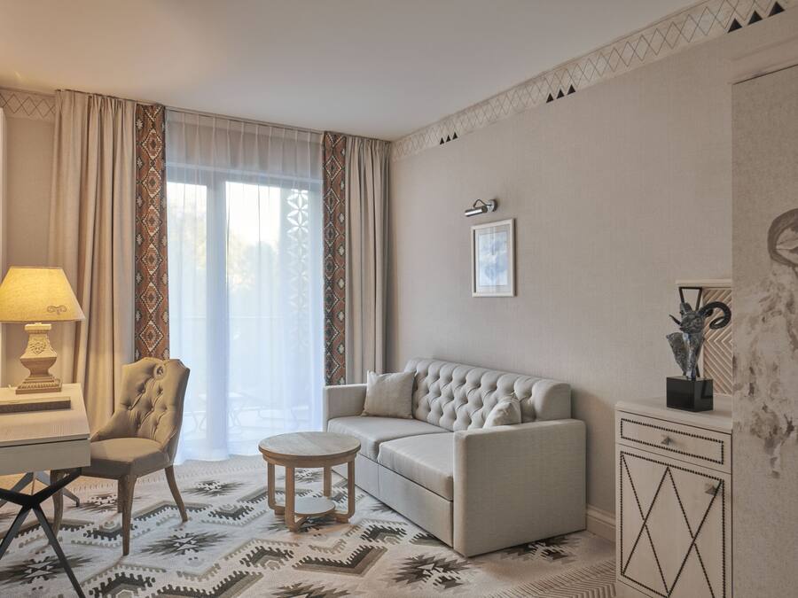 Una habitación de hotel con sofá, sillón, mesa redonda y un aparador decorativo.