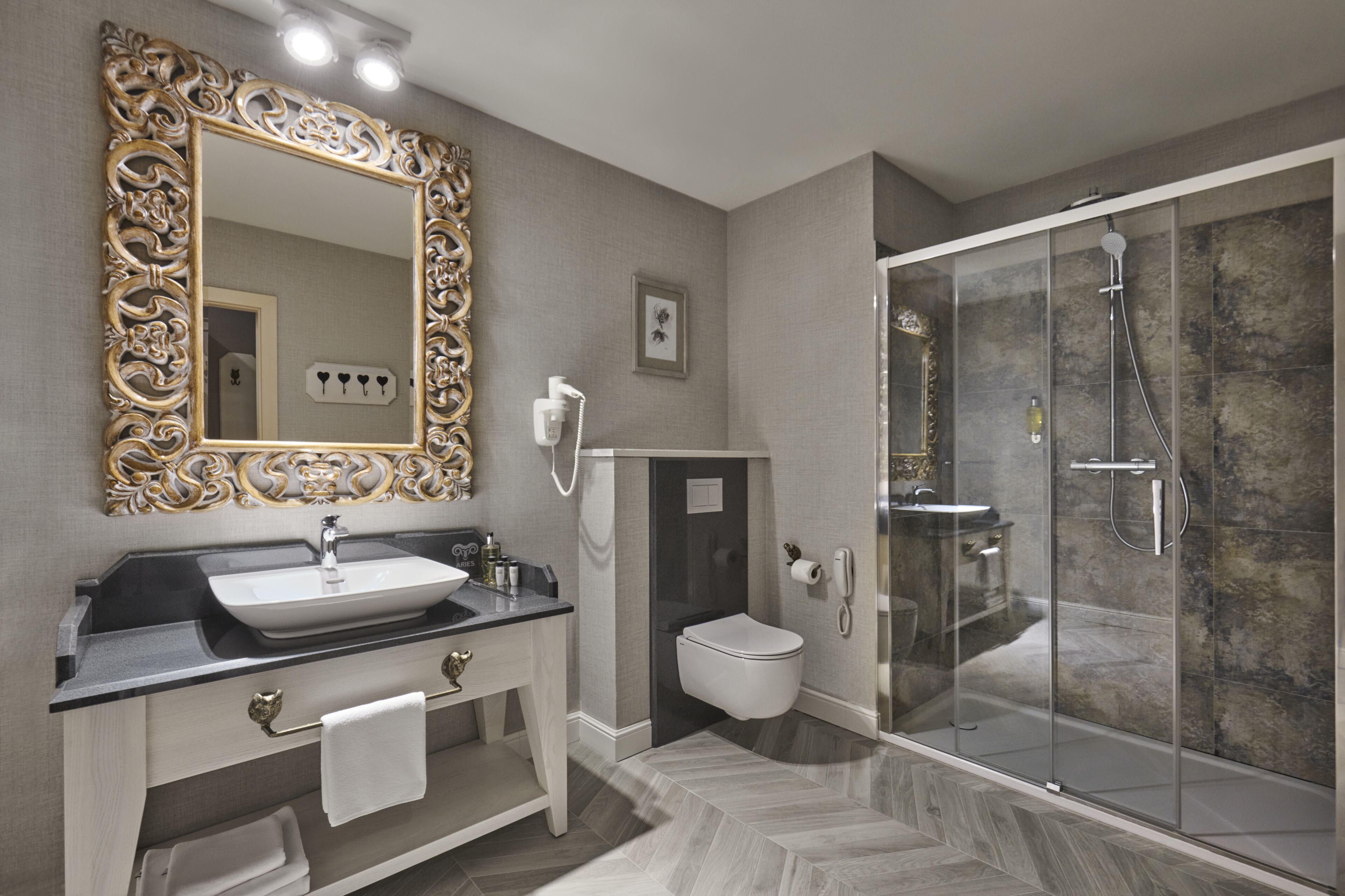 A modern bathroom with a large ornate mirror, a sink, vanity, toilet, and a glass-enclosed shower area.