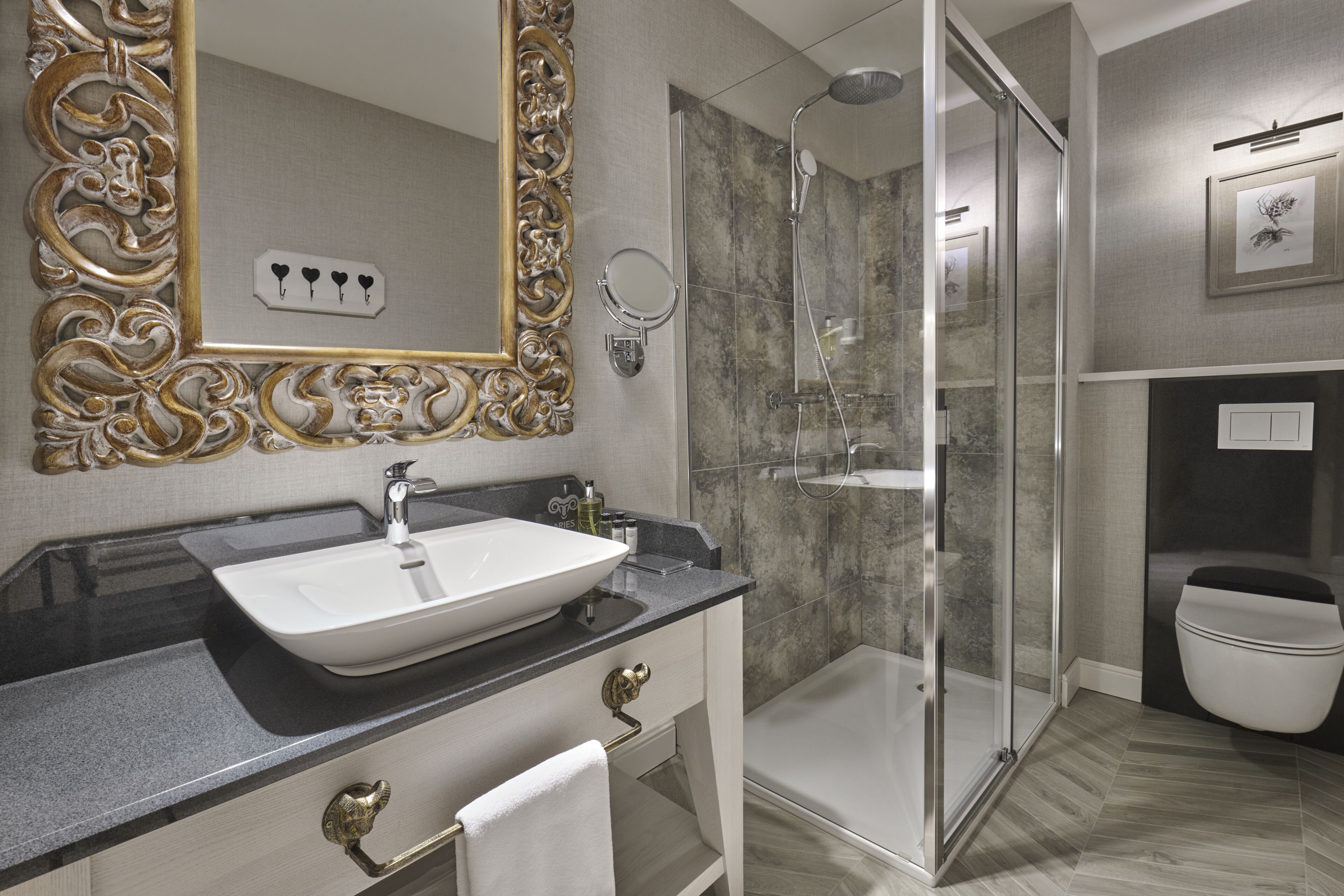 A modern bathroom with a large ornate mirror, a vessel sink, a glass-enclosed shower, and a toilet.
