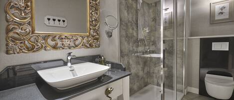 A modern bathroom with a large ornate mirror, a vessel sink, a glass-enclosed shower, and a toilet.