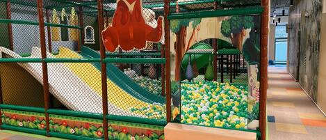 A children's play area with a slide, ball pit, and a large bear decoration.