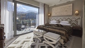 Un dormitorio espacioso con una cama grande, un balcón con vistas a las montañas y una alfombra estampada.