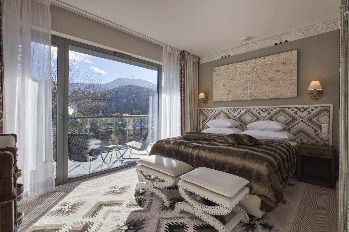 Un dormitorio espacioso con una cama grande, un balcón con vistas a las montañas y una alfombra estampada.