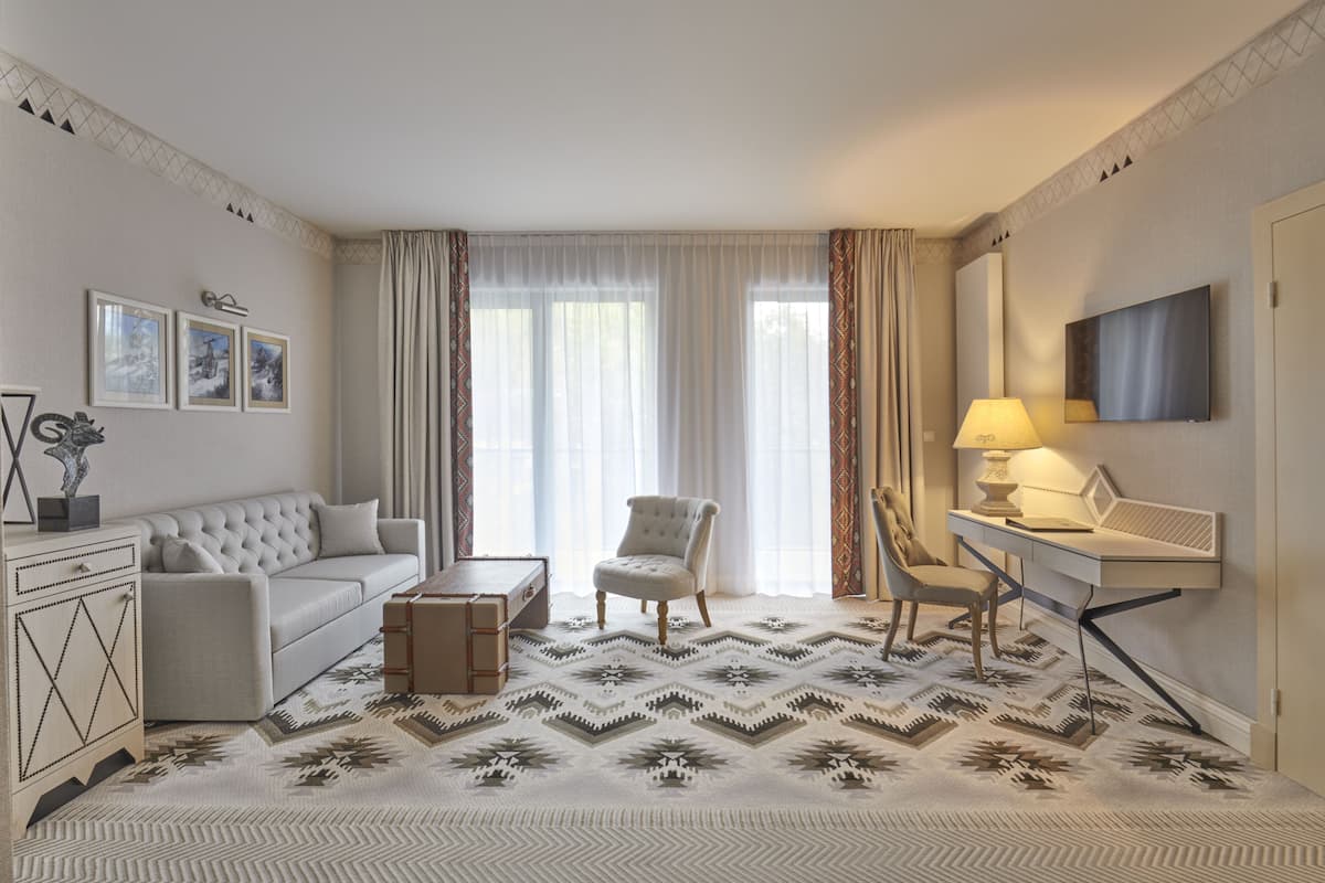 Habitación de hotel con sofá, sillón, escritorio y alfombra estampada.