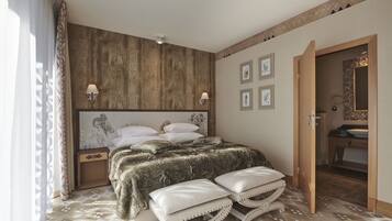 Quarto com cama grande, duas mesas de cabeceira, cabeceira, painel de parede em madeira, piso estampado e banheiro visível por uma porta aberta.