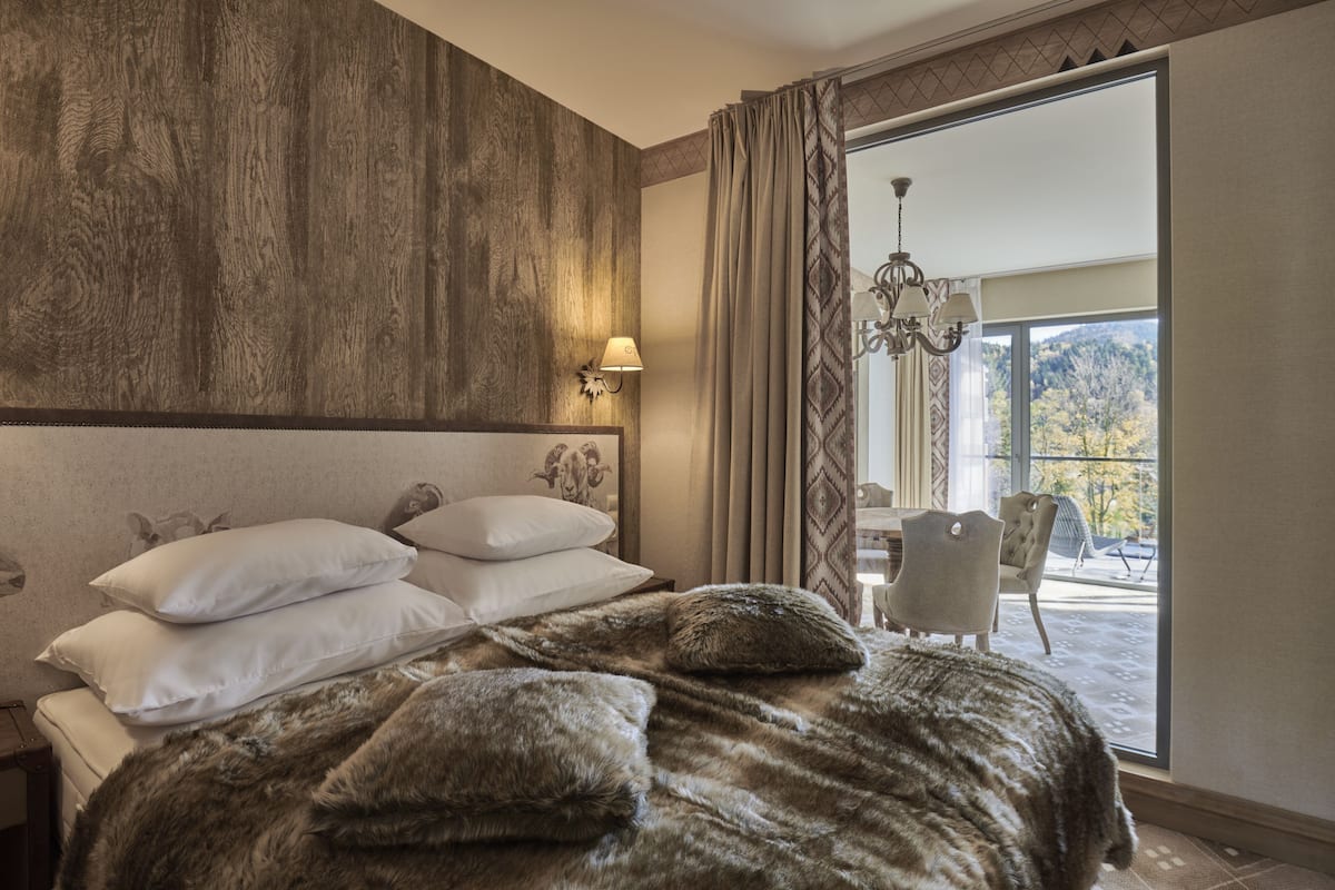 Un dormitorio con una cama grande, una araña de cristal y vistas a un balcón con sillas.